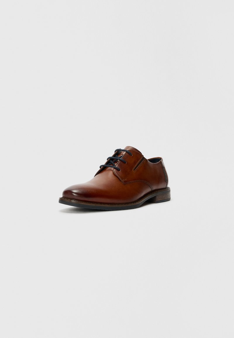 Zapato de vestir de cuero marrón con acabado suave, punta redonda y cordones negros. Presenta un tacón bajo apilado y sutilezas en la costura.