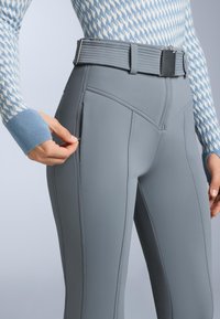 Grå sportleggings med hög midja, med sidsömmar och en ficka framtill. Materialet är slätt och elastiskt.