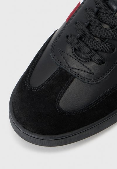 Sneaker nere con tomaia in pelle scamosciata e pelle, caratterizzate da accenti testurizzati, lacci neri e suola in gomma. Dettagli rossi sul lato.
