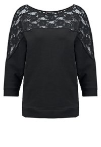 Haut noir à manches longues avec empiècement en dentelle sur le yoke et les épaules, encolure ronde et poignets ajustés.