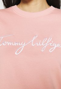 Sudadera rosa con cuello redondo acanalado, que presenta el logo bordado en blanco de "Tommy Hilfiger" en el pecho. Tela de algodón suave.