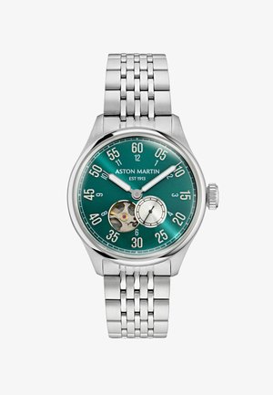 Hodinky Aston Martin so zeleným ciferníkom, strieborným kovovým remienkom, viditeľným ozubeným mechanizmom, veľkými minutovými značkami a malým subdialom pre sekundy.