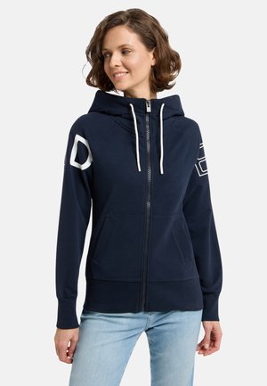Navy zip-up hoodie in soft material with a lined hood, white drawstrings, and large white letter detail on the left sleeve. Two front pockets.