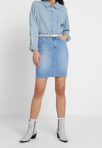 Ljusblå denimskjorta med långa ärmar, kombinerad med en ljusblå denimkjol. Bärs med vita ankelboots i ormtryck och ett mönstrat bälte.