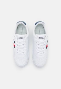 Białe sneakersy z gładką skórzaną powierzchnią, z czerwonymi i granatowymi paskami, perforowanym czubkiem, płaskimi sznurowadłami i wyściełanym kołnierzem.