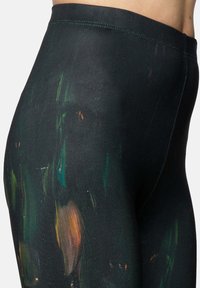 Zwarte leggings met een gestructureerd ontwerp en kleurrijke, abstracte verfschilderingen in groene, oranje en gele tinten op het oppervlak.