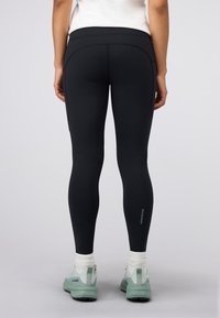Czarne, dopasowane legginsy wykonane z elastycznego materiału o gładkiej fakturze, z wysokim stanem i detalem logo w pobliżu kostki.