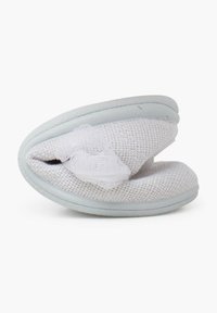 Zapatilla blanca con parte superior de tela texturizada y suela azul claro, ligeramente doblada. Presenta un delicado acento de encaje en el lado.