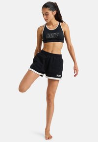 Sujetador deportivo negro con ribete blanco y gran logo "ROXY", combinado con pantalones cortos negros con detalles blancos y una cintura elástica.