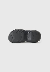 Black shoe sole featuring textured patterns, curved lines, and grooves for grip. Material appears rubbery with a smooth finish.