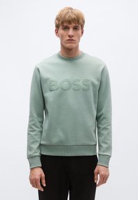 Világoszöld pulóver kerek nyakkivágással, elöl kiemelkedő "BOSS" logóval. Puha anyagból készült, bordázott mandzsettával és szegéllyel.