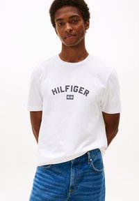 Witte katoenen t-shirt met een ronde hals en korte mouwen, voorzien van "HILFIGER" geborduurd in marineblauw over de borst. Draag het met blauwe jeans.
