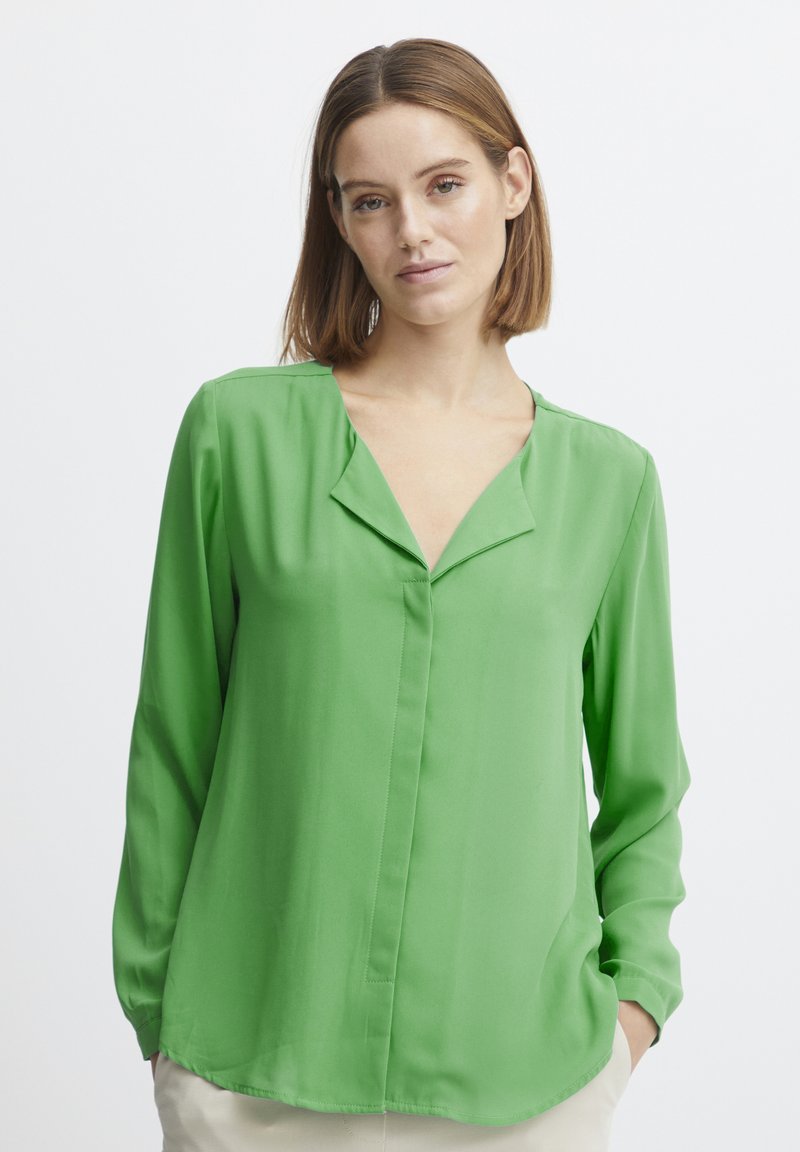 Green long-sleeve blouse in lightweight fabric, featuring a V-neck, front placket, and a curved hemline. Smooth texture and relaxed fit.
