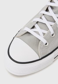 Gray canvas sneaker with white laces, rubber toe cap, and black outsole. Features metal eyelets and textured side panels.