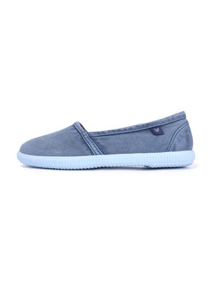 Zapato casual sin cordones en tela azul pizarra con suela de goma azul claro y una pequeña etiqueta lateral, mostrado desde el lado exterior sobre un fondo blanco.