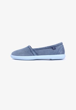 Zapato casual sin cordones en tela azul pizarra con suela de goma azul claro y una pequeña etiqueta lateral, mostrado desde el lado exterior sobre un fondo blanco.