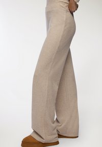 Beżowe, prążkowane spodnie szerokie z miękkiego materiału, z wysokim stanem i luźnym krojem. W połączeniu z brązowymi zamszowymi klapkami.