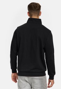 Pull noir à col montant, à manches longues et avec des poignets côtelés, fabriqué dans un matériau doux, présentant un design simple, sans motifs visibles.