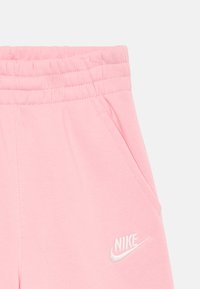 Pogled od blizu na roza Nike trenirke koje prikazuju elastični pojas, bočnu džepu i bele izvezene Nike logotip.