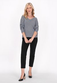 Pulover gri, cu decolteu în V și mâneci lungi, asociat cu pantaloni negri, strâmți și tocuri negre cu toc pătrat. Design simplu, fără modele.