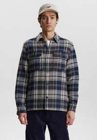 Plaid flannel shirt in navy, gray, and cream. Features two chest pockets and button closure, textured wool blend fabric.