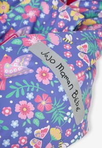 Borsa impermeabile con un design floreale viola, arricchito da uccelli e farfalle. Etichetta grigia con la scritta "JoJo Maman Bébé" in evidenza.