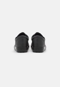 Schwarze Slipper aus glattem Lederoberteil, mit niedrigem Profil, flexibler Gummisohle und minimalen Nähten auf der Rückseite.