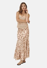 Top de ganchillo en beige sobre una falda maxi con volantes y estampado en tonos suaves de beige, combinado con sandalias planas. Tela suave y fluida.