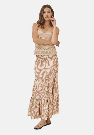 Top de ganchillo en beige sobre una falda maxi con volantes y estampado en tonos suaves de beige, combinado con sandalias planas. Tela suave y fluida.