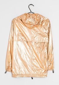 Metallisk guld regnjacka med huva, featuring en slät glansig textur, elastiska ärmmuddar och en framficka. Hänger på en svart krok.