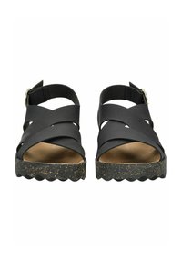 Černé sandály s křížovými pásky, platformou s korkovým vzhledem a vlnkovanou podrážkou. Nastavitelná spona na pásku kolem kotníku pro lepší přizpůsobení.