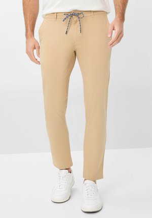 Beige lightweight pants with a drawstring waistband, slim fit, subtle sheen, and side pockets, paired with white sneakers.