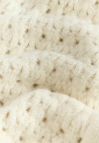 Tissu tricoté de couleur crème avec un motif texturé, présentant des points en relief de couleur brun clair. Fil doux et épais avec une apparence duveteuse.