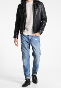 Veste en cuir noir avec une capuche en fourrure, pull en tricot crème, jeans déchirés bleu clair et bottines noires.