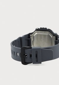 Bracelet de montre en caoutchouc gris avec des trous découpés, boucle noire et dos de boîtier en acier inoxydable, mettant en avant un design robuste et une esthétique moderne.