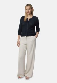 Granatowy kardigan prążkowany z zapięciem na guziki, zestawiony z kremowymi spodniami o szerokich nogawkach oraz sandałami na obcasie z odkrytymi palcami.