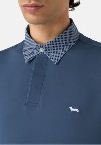 Polo blu navy con tessuto strutturato e colletto a fantasia. Presenta un logo decorativo di un bassotto bianco sul petto.
