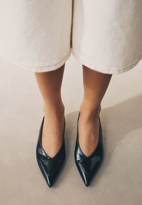 Mustad lakknahast terava ninaga kontsakingad sügava V-lõikega, mis näitavad läikivat viimistlust ja voolujoonelist siluetti.