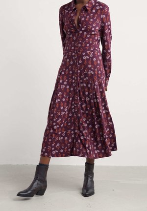 Robe longue à manches violettes avec imprimé floral orange et rose, boutonnée sur le devant, associée à des bottines noires et des chaussettes bleues.