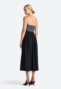 Rochie fără bretele, cu un corset gri cu elastic și o fustă fluidă neagră, completată cu mule cu toc negru. Textură netedă, design lungime ankle.
