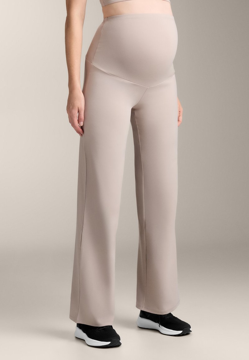 Pantaloni a palazzo per maternità in morbido tessuto beige, con vita alta, texture liscia e silhouette rilassata, abbinati a sneakers nere.