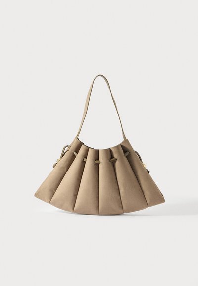 Sac à main en suede beige avec un design plissé, un détail à cordon de serrage et une bandoulière unique sur fond blanc.
