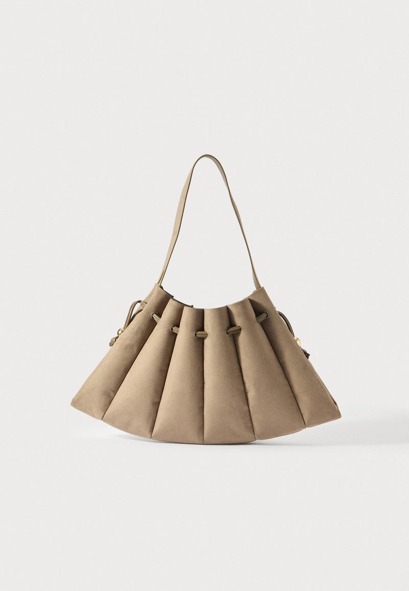 Beige semišová kabelka s skládacím designem, detaily na stahovací šňůrce a jedním ramenním popruhem na bílém pozadí.