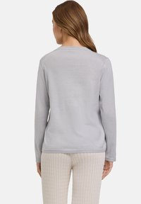 Helles grauer Langarmpullover mit rundem Halsausschnitt und geripptem Saum, kombiniert mit cremefarbener, strukturierter Hose mit Kabelstrickmuster.