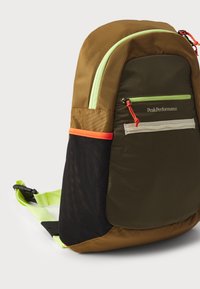Brown and green backpack with a front zip pocket, neon accents, mesh side pocket, and adjustable straps. Textured material with contrast stitching.