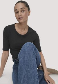 Zwarte t-shirt met korte mouwen en ronde hals, gecombineerd met losse blauwe denim jeans. Zittende pose, minimalistisch ontwerp, gladde textuur.