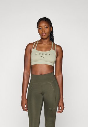 Green sports bra with thick adjustable straps and printed branding. Matched with high-waisted olive green leggings featuring seam detailing.