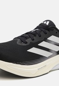Sort atletisk sko med en åndbar mesh-overdel, hvidt tre-stripes design, tekstureret sål med 'DREAMSTRIKE' detalje og sorte snørebånd.