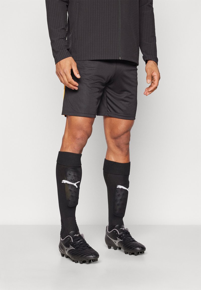 Black athletic shorts, long black socks with white logo, and black cleats. Textured long sleeve top, close-fitting design.