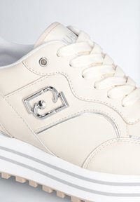Sneaker color crema con tomaia in pelle liscia, chiusura con lacci, dettagli in argento e suola bianca rialzata con strisce grigie.